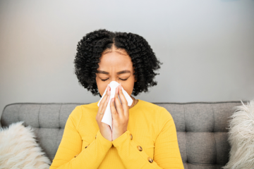 A woman with sinusitis blowing her nose on a couch